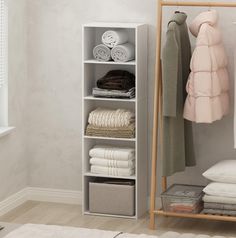 a white shelf filled with folded towels and blankets next to a window in a room