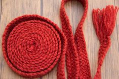 a red piece of yarn sitting on top of a wooden table next to a pair of scissors