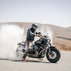 a man riding on the back of a motorcycle down a road next to a hill