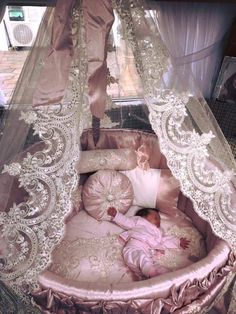 a baby is laying in a pink crib with white lace on the top and bottom