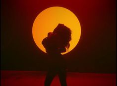 the silhouette of a woman in front of an orange and red sun with her hair blowing back