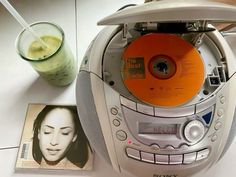 there is a cd player with an orange disc in it and a drink next to it