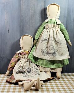 two cloth dolls sitting next to each other on a checkered tablecloth covered floor