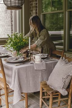 a woman sitting at a table in front of a window preparing to set the table