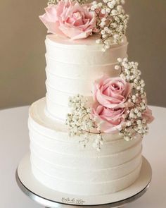 a three tiered white cake with pink roses on top and baby's breath