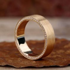 a gold ring with diamonds on top of a piece of wood next to a leaf