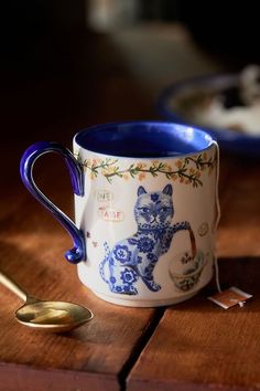 a blue and white coffee cup sitting on top of a wooden table next to a spoon