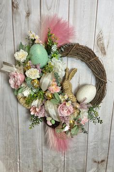 a wreath with flowers, feathers and an easter egg on the top is sitting against a wooden wall