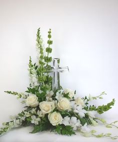 a cross with flowers and greenery in front of it on a white tablecloth