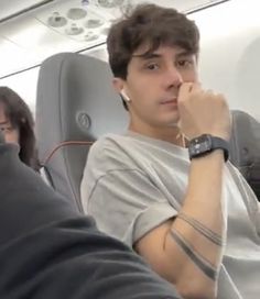 a young man sitting on an airplane with his arm around the other person's shoulder