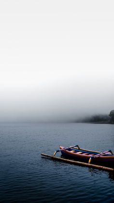 two canoes sitting on the water in front of a foggy lake with trees