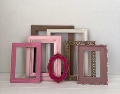 four different colored frames sitting next to each other on a white shelf in front of a wall