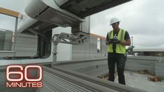 a man in yellow vest and hard hat standing on top of a metal conveyor belt