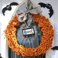 a halloween wreath made out of rolled up orange paper roses with boo eyes on the front door