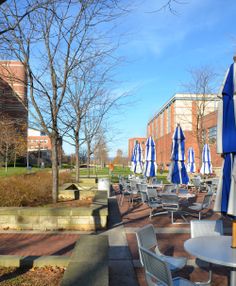 tables and chairs with blue umbrellas on the side walk in front of a brick building