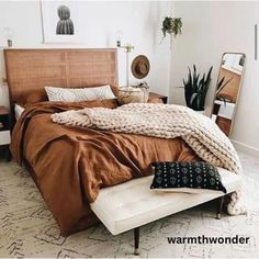 a bed with brown sheets and blankets on top of it in a room filled with plants