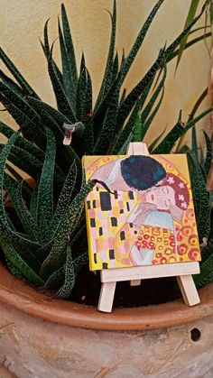 a miniature easel with a painting on it next to some succulents