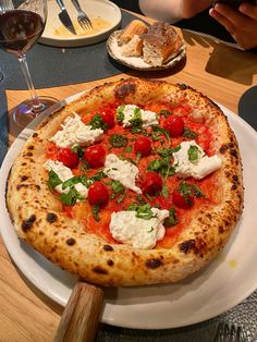 a pizza sitting on top of a white plate next to a glass of red wine