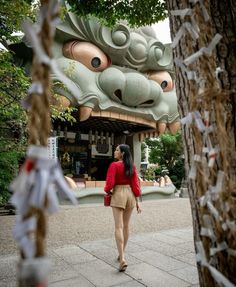 a woman walking down a sidewalk next to a tall dragon head sculpture on the side of a building