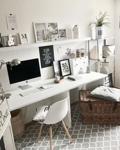 a white desk topped with a computer monitor next to a basket filled with pillows and blankets