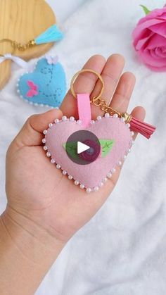 a hand holding a pink heart shaped keychain with a video playing on it