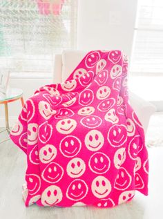 a pink and white blanket with smiley faces on it in front of a window,