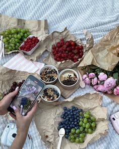 a person taking a photo of grapes, raspberries and other food on a bed