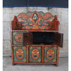 an old wooden cabinet with painted designs on the top and bottom, sitting in front of a brick wall