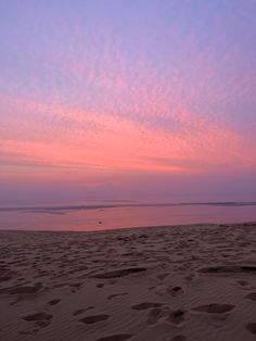 the sky is pink and purple as the sun sets in the distance on the beach