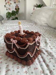 a crocheted cake sitting on top of a bed with a candle in it