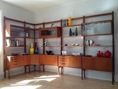 an empty room with wooden shelves and vases on top of the shelves, in front of a window