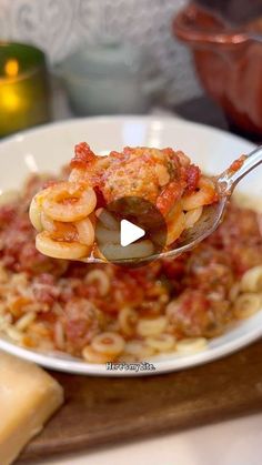 a spoon full of pasta with meat and sauce on it is being held by a person