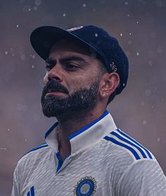 a man with a beard wearing a blue hat and white shirt is standing in the rain