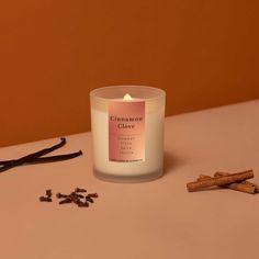 a glass candle sitting on top of a table next to cinnamon sticks and cloves