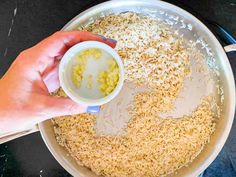 someone is mixing rice in a pan with a measuring cup on the side and one hand holding a spoon