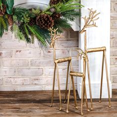 two gold reindeer statues next to a fireplace with pine cones and evergreens on the mantle