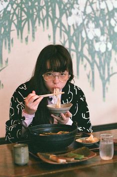 a woman sitting at a table eating food with chopsticks