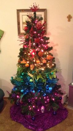 a brightly colored christmas tree with ornaments on it's base and lights in the top