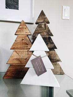 three wooden christmas trees sitting on top of a glass table next to a white wall