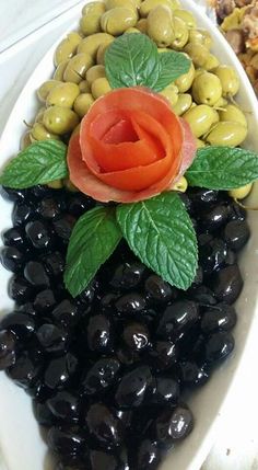 olives and green olives are arranged in a bowl with a rose on top