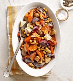 a white bowl filled with vegetables on top of a yellow and white towel next to a spoon