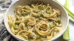 a bowl filled with pasta and broccoli sitting on top of a table next to celery