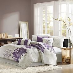 a bed with purple and white comforters in front of a large mirror on the wall