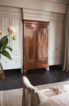 a bedroom with white cabinets and flowers in a vase on the floor next to a bed