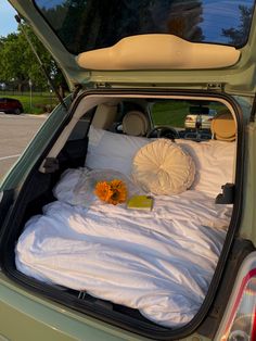 an open hatchback car trunk filled with white sheets and pillows next to a yellow flower