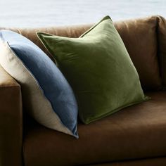 a brown couch with two green and blue pillows sitting on it's back end