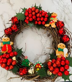 a christmas wreath with red berries, holly and teddy bears on the front is sitting on a marble surface