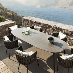 an outdoor dining table with chairs around it on a patio next to the ocean and mountains