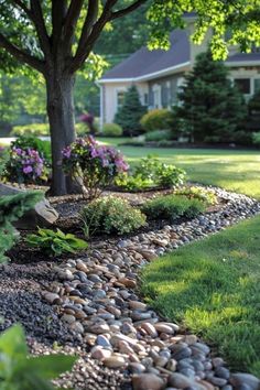 a garden with rocks and flowers in the grass next to a tree on a sunny day