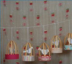 small birdcages hanging from a string with flowers on the wall in the background